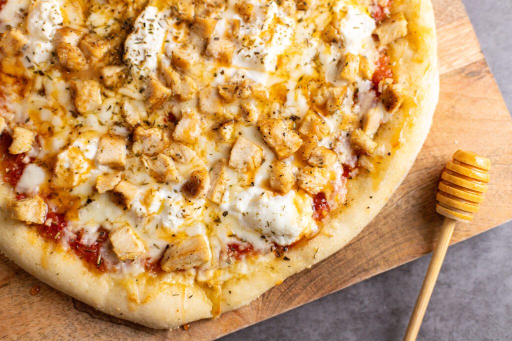 hot honey chicken pizza sitting on cutting board with honey wand