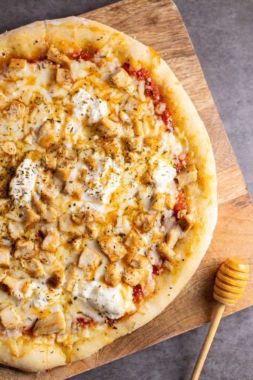 hot honey chicken pizza sitting on cutting board with a honey wand