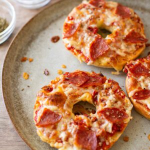 pepperoni pizza bagels sitting on a plate with seasonings