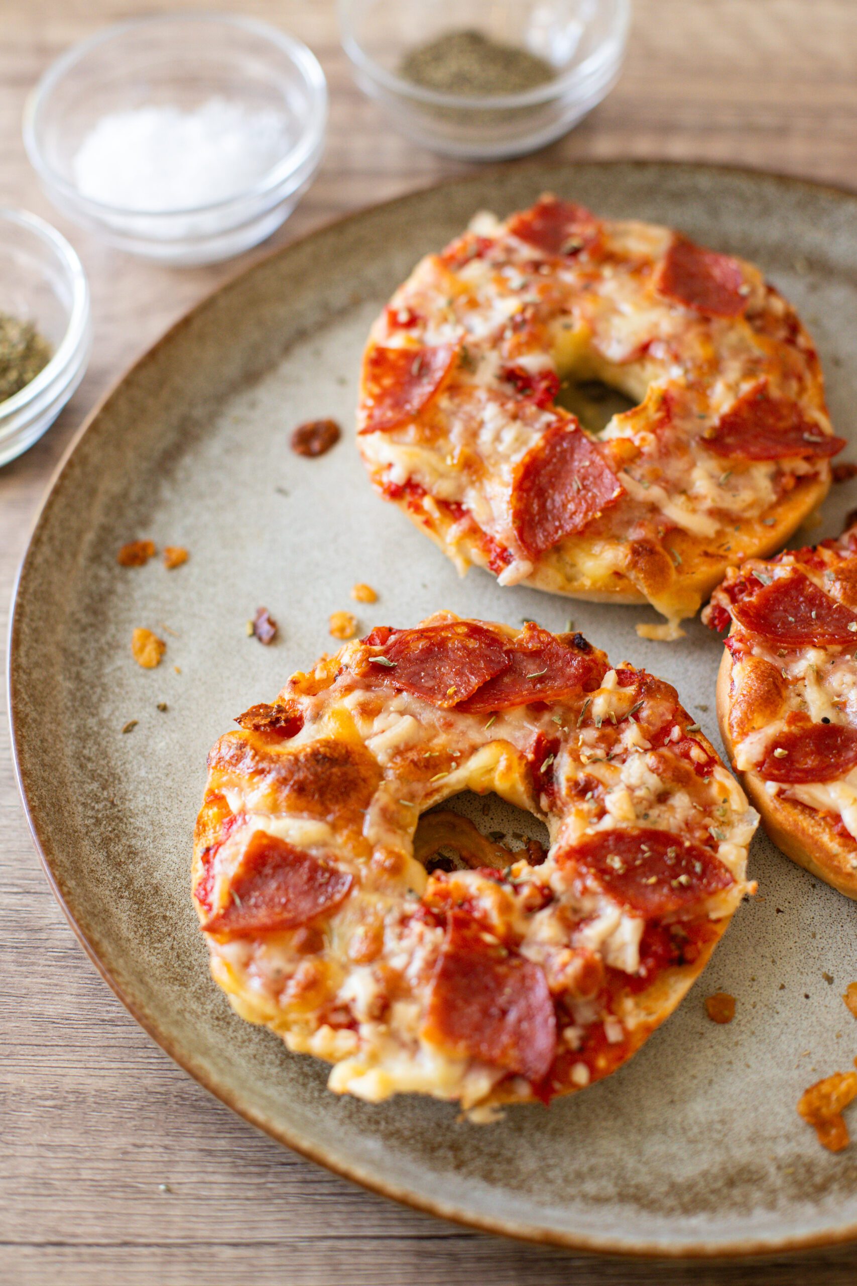 pepperoni pizza bagels sitting on a plate with seasonings