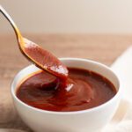 photo of a spoon dipping in a bowl of sweet and tangy bbq sauce