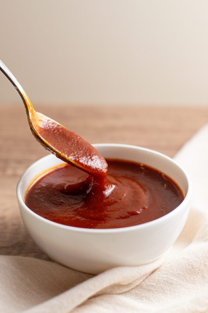 photo of a spoon dipping in a bowl of sweet and tangy bbq sauce