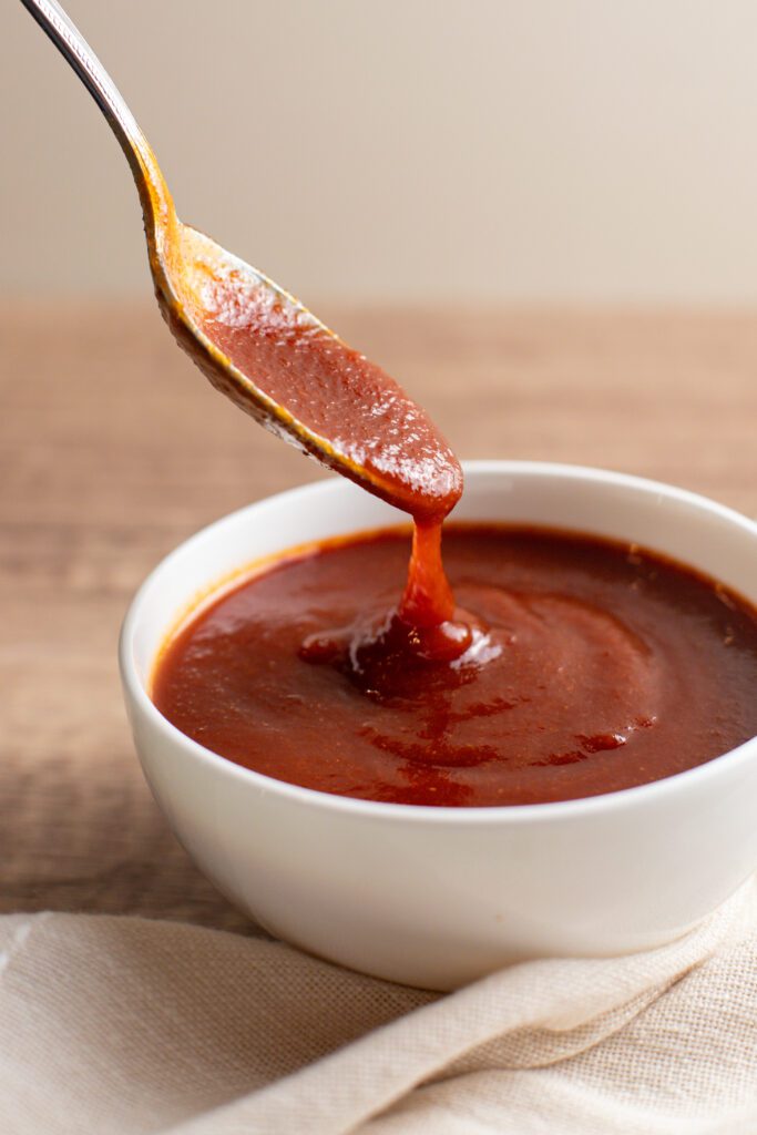 photo of a spoon dipping in a bowl of sweet and tangy bbq sauce