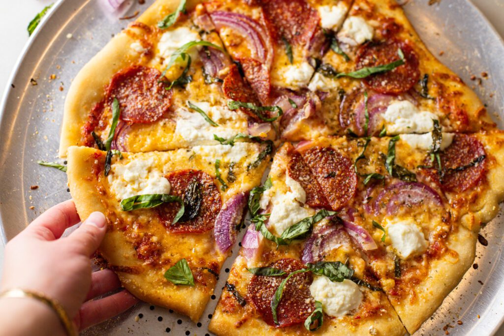 hand grabbing a slice of pizza from a pizza tray