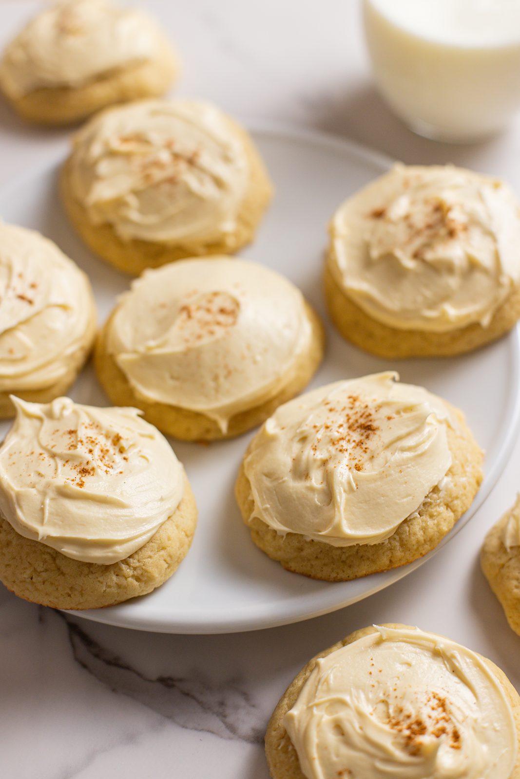 Sour cream cookies with maple buttercream frosting sitting on plate with milk