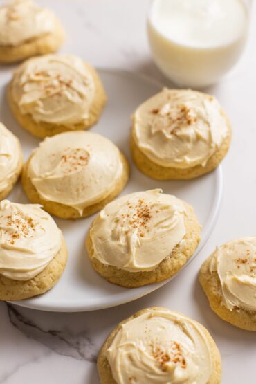 Sour cream cookies with maple buttercream frosting sitting on plate with milk