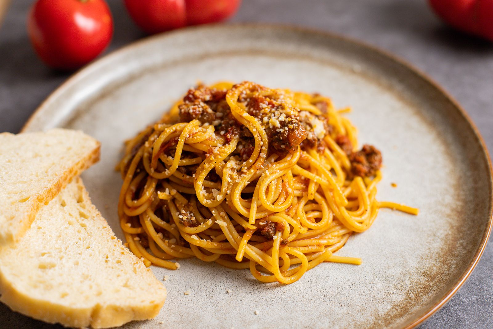 Slow cooked beef pasta sauce on a plate with tomatoes and bread