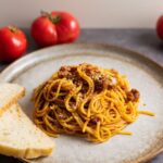 Slow cooker beef pasta sauce on a plate with tomatoes and bread