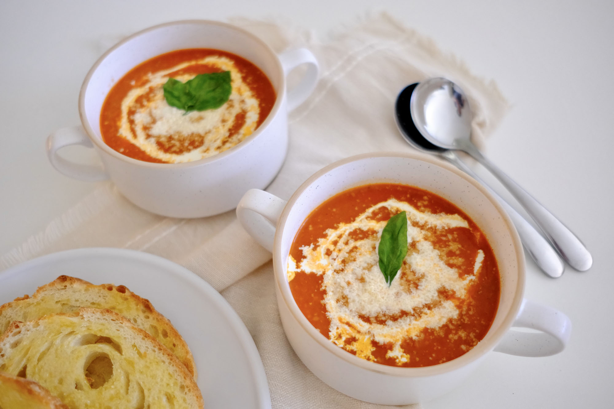 Bowl of roasted tomato vegetable soup topped with cream and fresh basil, served on a rustic wooden table.