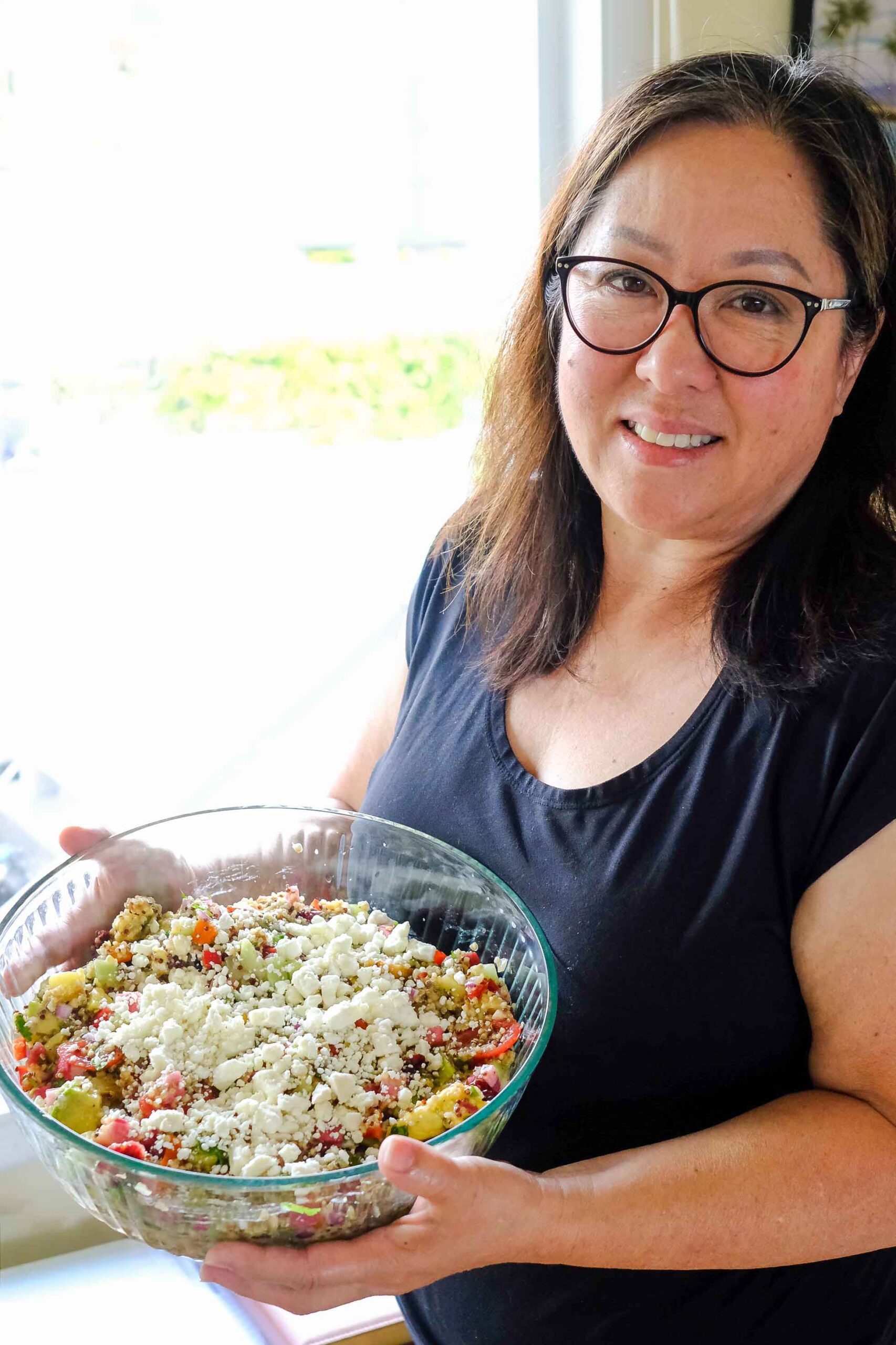 my mom holding a bowl of her rainbow quinoa salad, rainbow cucumber tomato quinoa salad in a bowl